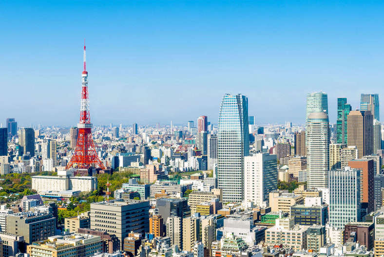 A panoramic view of Tokyo, featuring the Tokyo Tower amidst a skyline of modern skyscrapers under a clear blue sky.