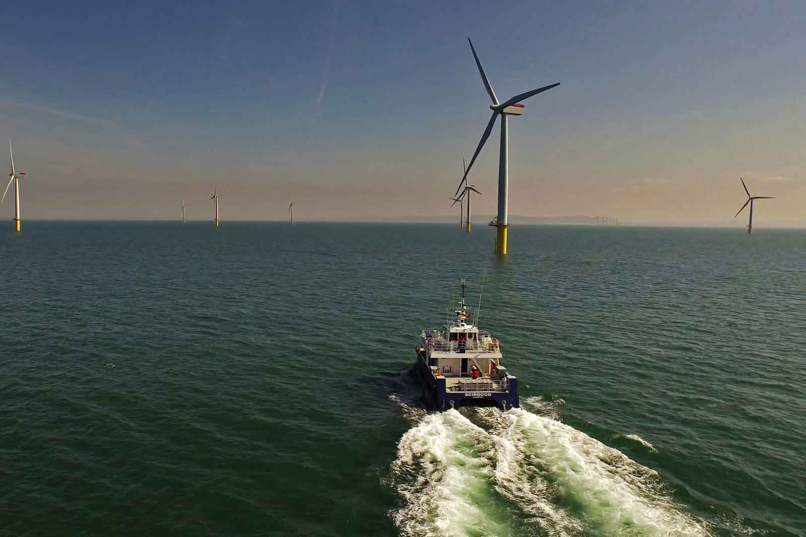 ボートが水を進み、晴れた空の下で海上風力タービンに囲まれています。