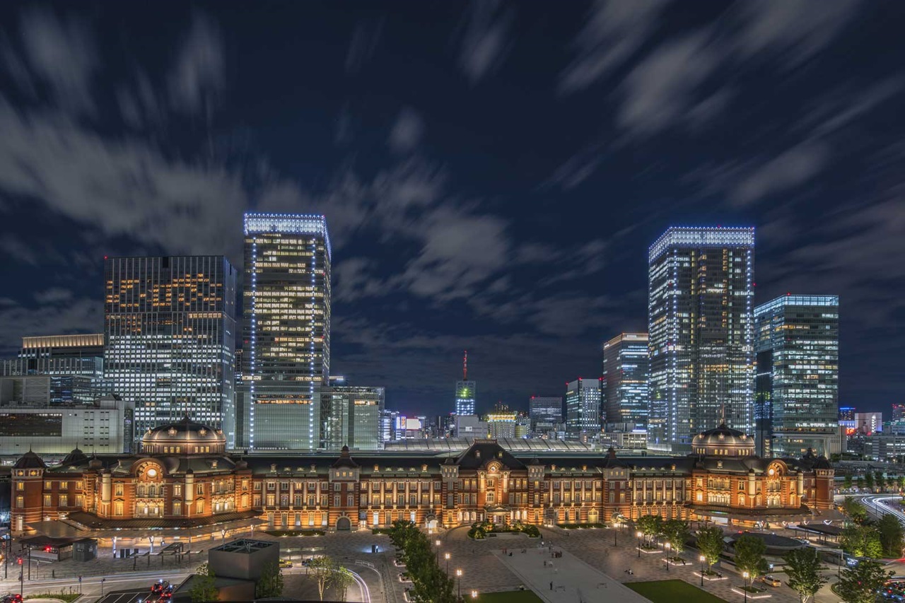 夜の東京駅のビュー、背景には近代的な高層ビルと照明された雲があります。