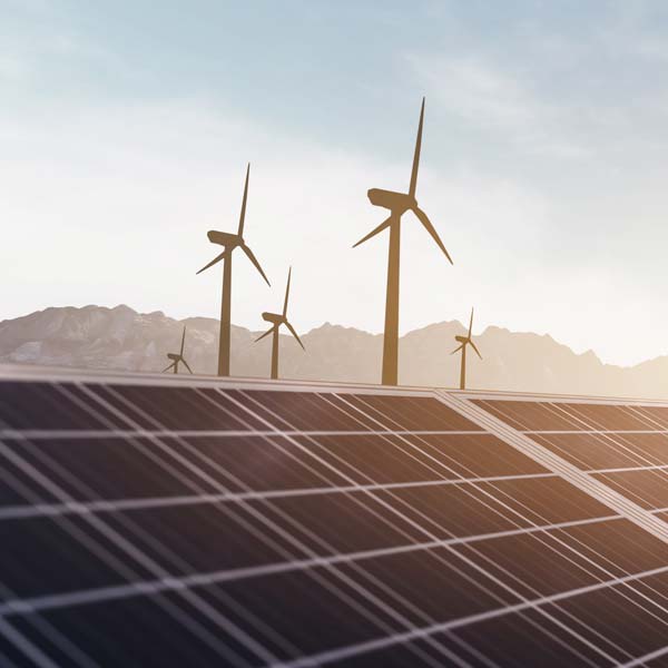 Wind turbines are seen behind solar panels under a clear sky, showcasing renewable energy solutions.