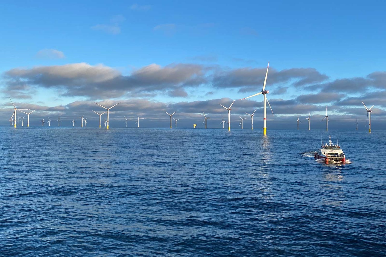 An offshore wind farm with multiple wind turbines and a boat navigating through the calm water.