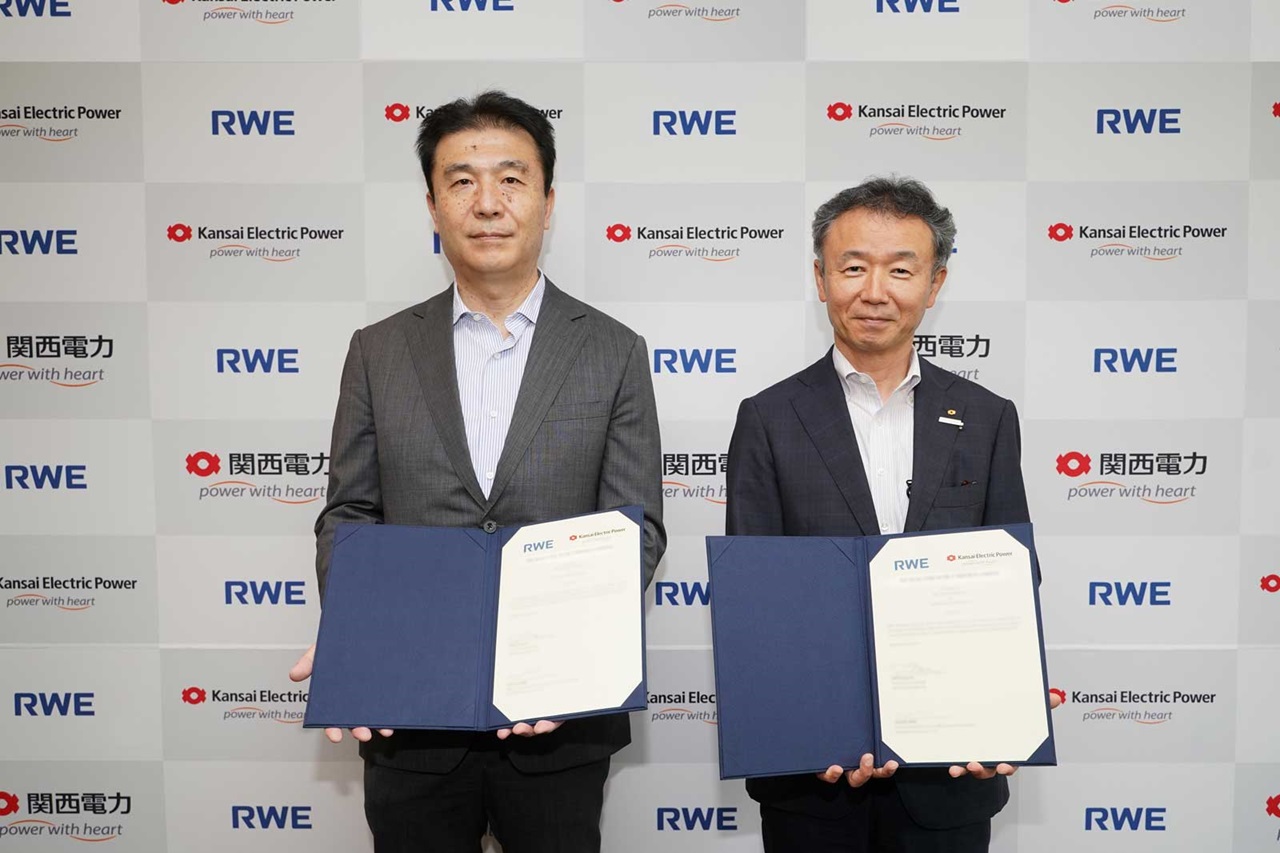 二人が関西電力とRWEのロゴがある壁の前で書類を持っています。