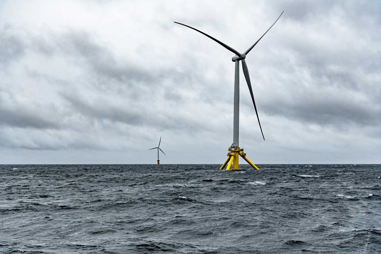二つの洋上風力発電機が曇った空の下、荒れた海に立っています。